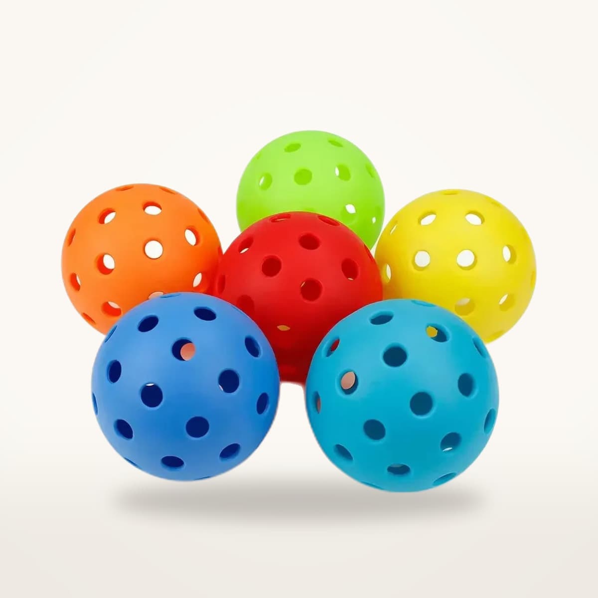 Six balles de pickleball d'extérieur de couleurs différentes, percées de petits trous, groupées sur fond neutre
